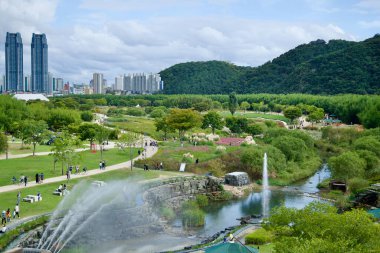 Ulsan, Güney Kore - 5 Ekim 2024: Taehwa Nehri Ulusal Bahçesi 'ndeki yönetim binasının üst katından panoramik bir manzara, bahçenin havuzu, çeşmeleri, yürüyüş yolları ve uzak şehir manzarasını gözler önüne seriyor..