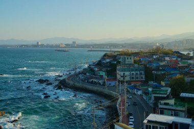 Gangneung Şehri, Güney Kore - 3 Kasım 2024: Tarihi Jumunjin Deniz fenerine bakan Jumunjin Limanı, dolambaçlı kıyı yolu, canlı binalar ve geniş Doğu Denizi manzaralı.