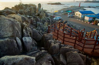 Goseong County, Güney Kore - 3 Kasım 2024: Ahşap merdivenler Neungpadae 'nin kayalık arazisinden Doğu Denizi kıyısındaki engebeli sahil şeridi ve deniz feneri manzaralı bir park alanına iniyor..