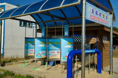 Sokcho, Güney Kore - 3 Kasım 2024: Sokcho Sahili 'nde sikke işleten duş kabinleri ziyaretçilere kolaylık sağlıyor, renkli tabelalar ve mavi bir gölgelik altında modern bir açık hava yıkama istasyonu bulunuyor..
