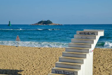 Sokcho, Güney Kore - 3 Kasım 2024: Arka planda Jodo Adası ile birlikte Sokcho Sahili 'ne çıkan tahta merdivenler. Kumlu kıyıya vuran dalgalarla sakin bir sahne..