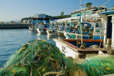 Sokcho, South Korea - November 3, 2024: A close-up of green fishing nets with bright yellow floats, set against docked fishing boats at Seorak Port, showcasing the active local fishing industry. clipart