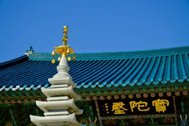 Yangyang County, South Korea - November 3rd, 2024: A close-up of the golden finial on the stone pagoda in front of Botajeon Hall at Naksansa Temple, with the ornate temple roof in the background. clipart