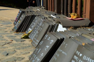 Yangyang County, South Korea - November 3, 2024: Rows of traditional roof tiles with handwritten messages of hope and prayer, left by visitors at Naksansa Temple as part of a cultural tradition. clipart