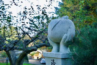 Yangyang County, South Korea - November 3rd, 2024: A stone sculpture of hands holding an apple near Hongye Gate at Naksansa Temple, set against a backdrop of trees and serene greenery. clipart