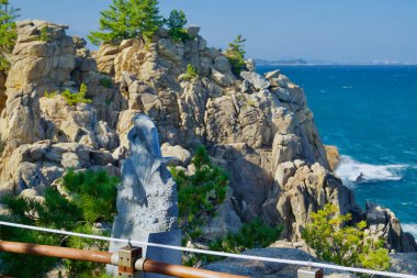 Yangyang İlçesi, Güney Kore - 3 Kasım 2024: Gisamun Deniz fenerinden kuzeye doğru manzaralı bir manzara, ön planda bir yunus heykeli ve engebeli sahil kayalıkları ve arka planda Doğu Denizi yer alıyor.