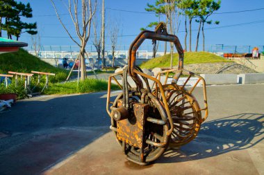 Yangyang County, South Korea - November 3rd, 2024: A rusted piece of fishing equipment is displayed as a cultural artifact near Namae Port, set against a backdrop of greenery and a sunny sky. clipart