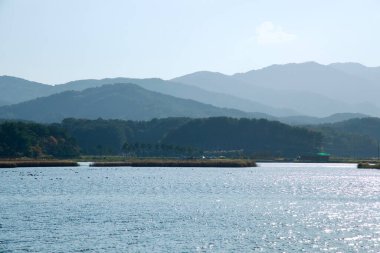 Yangyang İlçesi, Güney Kore - 3 Kasım 2024: Pomae Gölü 'nün güneşli suları, berrak bir sonbahar gününde katmanlı orman tepeleri ve uzak dağlara karşı parıldıyor.