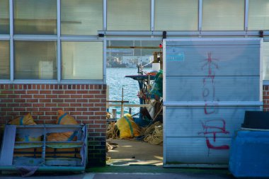 Yangyang County, South Korea - November 3rd, 2024: A peek through a doorway reveals the bustling docks of Namae Port, with fishing equipment, boats, and the glistening waters of the East Sea in the background. clipart