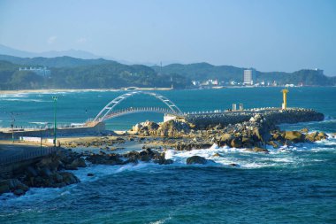 Yangyang İlçesi, Güney Kore - 3 Kasım 2024: Yangyang Namae Güneş Doğumu Gözlemevi, çarpıcı beyaz kemeri ve sarı feneriyle, Namae Limanı Skywalk 'tan görülen Doğu Denizi dalgalarına karşı durmaktadır..