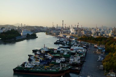 Ulsan, South Korea - November 14, 2024: A serene dusk view of Jangsaengpo Port with rows of docked vessels and the sprawling Yongyeon Industrial Complex, framed by chimneys emitting soft plumes. clipart