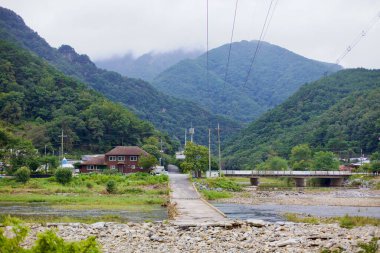 Goesan İlçesi, Güney Kore - 9 Eylül 2020: Chilseong Kasabası 'ndaki Ssang Nehri' ni geçen dar bir köprü orman tepelerine yapışmış, yemyeşil bir dağ vadisine kurulmuş küçük bir köye çıkıyor..
