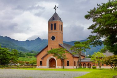 Goesan İlçesi, Güney Kore - 10 Eylül 2020: Yeonpung Kutsal Toprak Katedrali, Katolik şehitleri onurlandırmak için inşa edilen kırmızı tuğlalı kilise Sobaek Dağları 'nın puslu zirvelerine karşı durarak bir yansıma ve inanç yeri sunuyor..