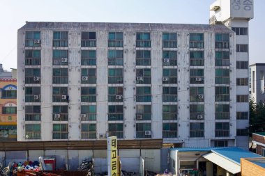 Sejong City, South Korea - November 12, 2020: An older apartment building in Jochiwon shows signs of wear, with weathered walls, air conditioning units on balconies, and a recycling yard in the foreground. clipart