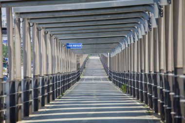 Sejong City, Güney Kore - 26 Mayıs 2021: Kuzey Yıldızı Yolu boyunca güneş enerjisiyle kaplı bisiklet yolunun uzun bir uzantısı, üst panellerden gelen gölgeler kaldırımda bir desen oluşturuyor. Yol, yenilenebilir enerjiyi kentsel hareketlilikle bütünleştirir.