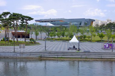 Sejong Şehri, Güney Kore - 26 Mayıs 2021: Arka planda Sejong Kongresi Merkezi 'nin modern mimarisinin yer aldığı Sejong Gölü Parkı' nın ağaçlandırılmış yürüyüş yolları ve açık plazalarıyla manzarası.