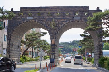 Gongju, South Korea - May 27, 2021: A large Baekje-style archway marks the entrance to downtown Gongju, featuring traditional design elements, engraved inscriptions, and a decorative emblem. clipart