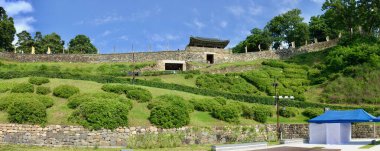 Gongju Gongsanseong Kalesi 'nin panoramik manzarası Geumseoru Kapısı, taş duvarlar, yemyeşil manzara ve ön planda geçici bir çadır..