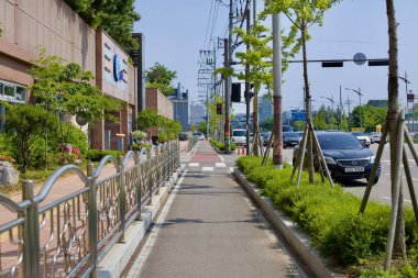 Gunsan, Güney Kore - 28 Mayıs 2021: Gunsan şehir merkezinde yeşil, modern altyapı ve bisikletçiler ve yayalar için kentsel peyzaj ile kaplı yoğun bir yolun yanında iyi korunan bir bisiklet yolu bulunmaktadır..
