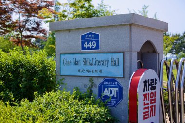 Gunsan, South Korea - May 28, 2021: A stone entrance sign marks the location of Chae Man-Sik Literary Hall, dedicated to the renowned Korean writer, set among lush greenery along Gangbyeon-ro. clipart