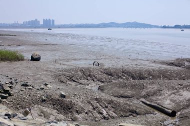 Gunsan, Güney Kore - 28 Mayıs 2021: Geum Nehri 'nde alçak gelgit sırasında geniş bir çamur tabakası, dağınık enkaz, gelgit kanalları ve şehrin ufuk çizgisine karşı uzak balıkçı tekneleri ortaya çıkar..