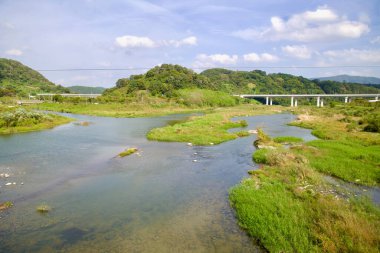 Imsil İlçesi, Güney Kore - 4 Ekim 2021: Seomjin Nehri, kırsal bölgeleri ve bisiklet rotalarını birbirine bağlayan, modern bir köprü gibi, küçük çimli adaları olan yemyeşil bir sulak alan boyunca akar..