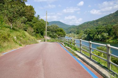 Seomjingang Bisiklet Yolu 'nun dolambaçlı bir bölümü yemyeşil ve yuvarlanan tepelerle çevrili nehirleri takip ederek bisikletlilere manzaralı ve huzurlu bir yolculuk sunuyor..