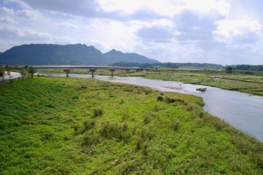 Sunchang İlçesi, Güney Kore - 4 Ekim 2021: Seomjin Nehri boyunca uzanan bir köprü, bereketli, yeşil vadiyi uzaktaki dağlarla birleştirerek, bulutlu bir gökyüzünün altında, sakin manzaranın üzerine yumuşak bir ışık saçar..