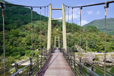 Sunchang County, Güney Kore - 4 Ekim 2021: Seomjin Nehri üzerinde uzanan Janggunmok Askı Köprüsü 'nün perspektif görüntüsü, arka planda yemyeşil dağlar tarafından çerçevelenmiş ziyaretçiler yürüyor.