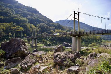 Sunchang İlçesi, Güney Kore - 4 Ekim 2021: Janggunmok Askı Köprüsü Seomjin Nehri boyunca uzanır, engebeli kaya oluşumları ve bereketli dağ manzaralarıyla çevrili, ziyaretçiler ve bisikletçiler için manzaralı bir geçiş sağlar..
