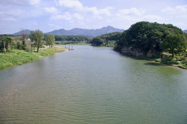 Sunchang County, Güney Kore - 3 Ekim 2021 Seomjingang Bisiklet Yolu boyunca manzara yaratan yemyeşil bir nehir, küçük bir rıhtım ve uzak dağlar..