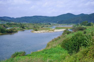 Namwon Şehri, Güney Kore - 3 Ekim 2021: Seomjin Nehri kırsal alanda eserek, kendi rotası boyunca küçük adalar ve kumsallar oluşturur. Bereketli yeşillik ve uzak dağlar durgun suları çevreledi..