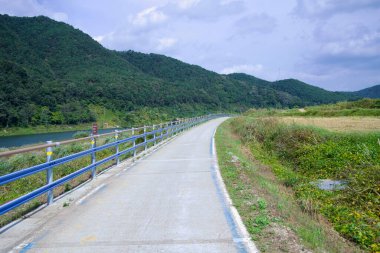 Namwon Şehri, Güney Kore - 3 Ekim 2021: Seomjingang Bisiklet Yolu 'nun sakin bir bölümü, yemyeşil dağlarla çevrili nehri takip ederek bisikletçilere manzaralı bir yol sunuyor..