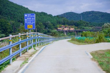 Namwon Şehri, Güney Kore - 3 Ekim 2021 Seomjingang Bisiklet Yolu 'nda bir yön işareti Seomjingang Barajı ve Gumi-gyo Köprüsü' nü gösteriyor, arka planda Hyangga Lunaparkı ve demiryolu köprüsü var..