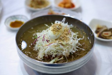 Gurye County, Güney Kore - 3 Ekim 2021: Bir kase naengmyeon, Kore usulü soğuk erişte dilimlenmiş lahana, haşlanmış yumurta ve susam tohumuyla servis edilir. Bu ferahlatıcı yemek Kore mutfağının temel öğesidir, özellikle sıcak havalarda..