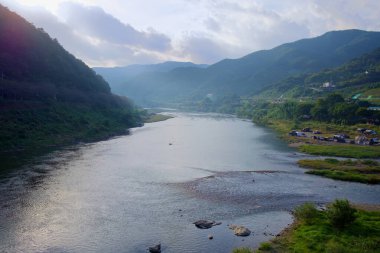 Gurye County, Güney Kore - 3 Ekim 2021 Seomjin Nehri 'nin sisli bir sabah manzarası, yemyeşil tepeler ve Apnok Resort kıyısında küçük bir kamp alanı ile kaplı nehir kıyıları..