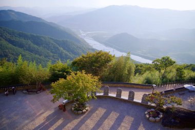 Gurye İlçesi, Güney Kore - 3 Ekim 2021: Saseongam Hermitage 'den sakin bir manzara, Seomjin Nehri' nin yemyeşil dağlarda dolaşmasını, taştan koruyucu heykellerin öğleden sonra aydınlığında uzun gölgeler bırakmasını..