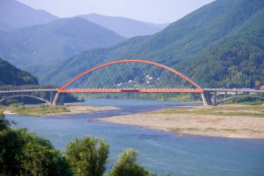 Gurye İlçesi, Güney Kore - 3 Ekim 2021: Namdo Köprüsü, belirgin kırmızı ve mavi kemerleriyle Seomjin Nehri boyunca uzanır, Gurye ve Hadong 'u yemyeşil dağ manzarasının ortasına bağlar..