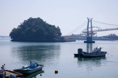 Gwangyang, Güney Kore - 3 Ekim 2021: Baealdo 'yu anakaraya bağlayan Byeol Heneun Köprüsü manzaralı bir manzara, Seomjin Nehri ile Güney Denizi' nin birleştiği sakin sularda yüzen balıkçı tekneleri..