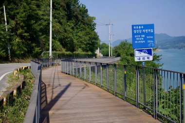 Gwangyang Şehri, Güney Kore - 3 Ekim 2021: Seomjin Nehri boyunca dolambaçlı ahşap bisiklet yolu bisikletçiler için manzaralı ve güvenli bir rota sağlar. İşaretler, Seomjingang Bisiklet Yolu 'ndaki kilit noktalara% 7' lik bir düşüş ve mesafeyi gösteriyor..