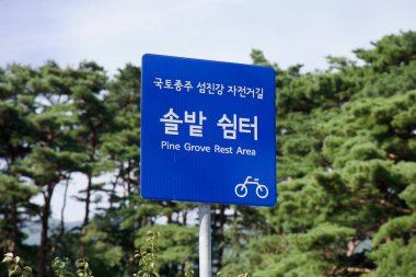 Gwangyang Şehri, Güney Kore - 3 Ekim 2021 Seomjingang Bisiklet Yolu üzerindeki Pine Grove Dinlenme Alanı 'nı gösteren mavi bir işaret, verimli bir çam ormanının ortasında bisikletçiler için belirlenmiş bir durak sağlıyor..
