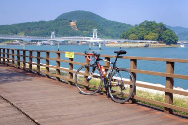 Gwangyang, Güney Kore - 3 Ekim 2021: Seomjingang Bisiklet Yolu 'nun bir parçası olan Haemaji Köprüsü ve Baealdo Adası' na bakan manzaralı bisiklet yolunun ahşap korkuluğuna yaslanan bir yol bisikleti.
