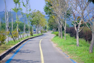 Gwangyang, Güney Kore - 3 Ekim 2021 Seomjingang Bisiklet Yolu 'nun kıvrımlı bir bölümü genç ağaçlarla kaplı, bisikletçilere Seomjin Nehri boyunca manzaralı ve gölgeli bir yol sunuyor..