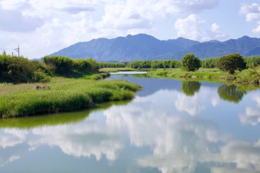 Damyang County, Güney Kore - 23 Eylül 2020 Yeongsan Nehri 'nin sakin bir bölümü yemyeşil ve uzak dağlarla çevrili, gökyüzünde sürüklenen beyaz bulutları yansıtır..