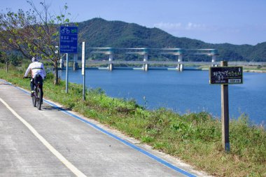 Naju Şehri, Güney Kore - 24 Eylül 2020: Bisikletçiler Juksan Weir yakınlarındaki Yeongsangang Bisiklet Yolu boyunca yol bulma işaretleriyle kilit noktalara ve Juksanbo Sertifika Merkezine olan mesafeleri takip ediyorlar..