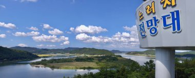 Neureoji Gözlem Merkezi işareti önde duruyor, Yeongsan Nehri ikonik U-şekli, yemyeşil tepeler ve uzak dağların çarpıcı panoramik manzarasını çerçeveliyor..