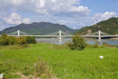 Muan County, Güney Kore - 25 Eylül 2020: Nehir boyunca uzanan Muyeong Köprüsü 'nün çarpıcı manzarası, yeşil tepeler ve gür bitki örtüsüyle çerçevelenmiş, modern köprü yapısına barışçıl bir tezat sunuyor..
