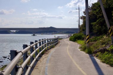 Muan County, Güney Kore - 25 Eylül 2020: Yeongsangang Bisiklet Yolu 'nun dar bir bölümü nehir boyunca ilerliyor, modern bir köprünün altından geçiyor, güvenlik korkulukları ve elektrik direkleriyle yolu kapatıyor..