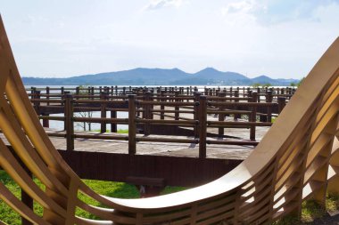 Muan County, Güney Kore - 25 Eylül 2020: Yeongsan Nehri üzerinde uzanan ahşap bir gözlem güvertesi, modern ahşap yapının kıvrımlı kenarları tarafından çerçevelenmiş, su ve uzak dağların panoramik manzarasını sunuyor..