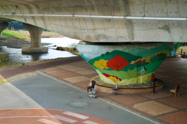 Ulsan City, Güney Kore - 31 Mart 2025: Taehwa Nehri köprüsünün altındaki el boyaması destek sütununu çevreleyen çeşitli sandalyeler, alanı nehir kenarında gayri resmi bir dinlenme yerine dönüştürüyor..
